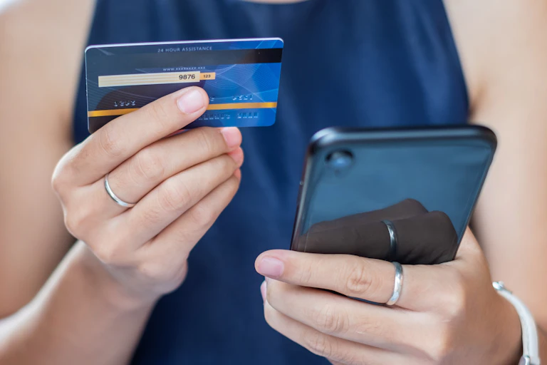 A woman holds a credit card in one hand and a smart phone in the other