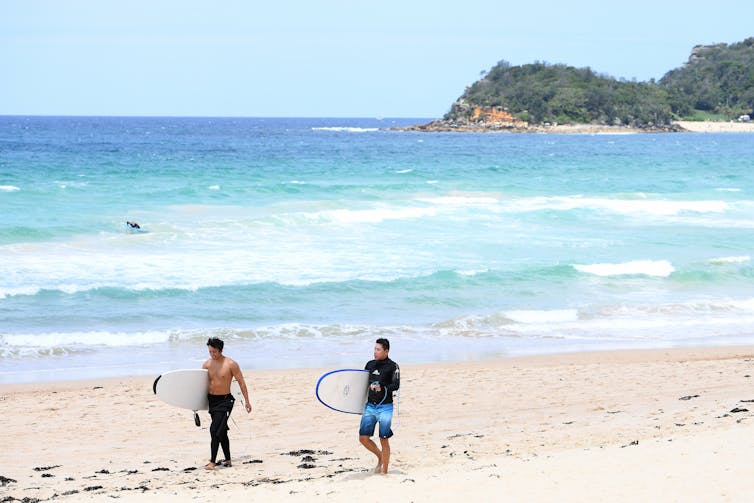 Surfers walk along a Sydney beach.