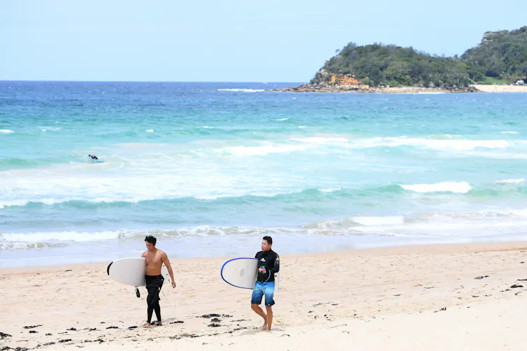 Surfers walk along a Sydney beach.