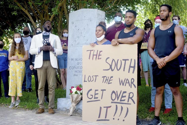 Crowd of young people stands by Walker County's Confederate monument with signs saying, 'The South lost the war, get over it!'