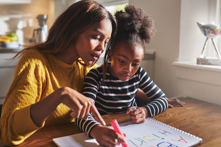 Woman in yellow jumper helping child in striped jumper with homework