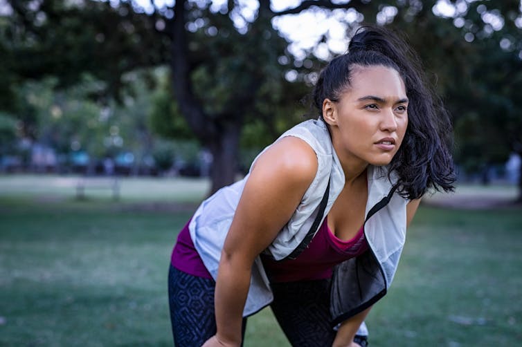 A woman in a park in exercise clothes bends down to rest