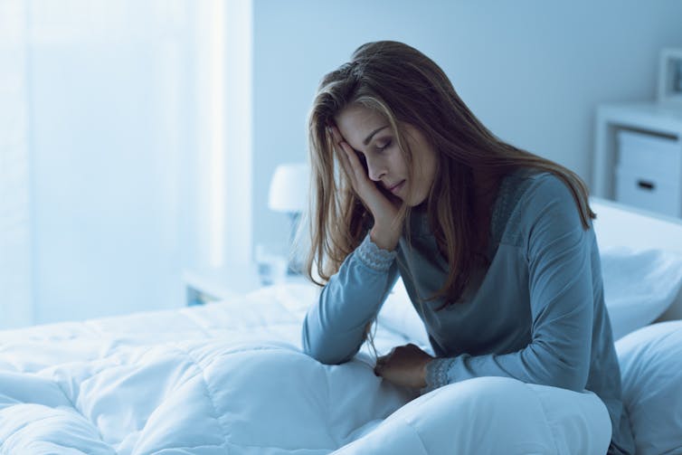 A woman sitting up in bed with head in hand.