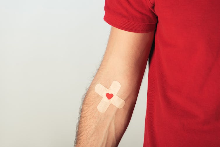 Person in red T-shirt wearing a criss-cross plaster and a red heart symbol over it on their arm
