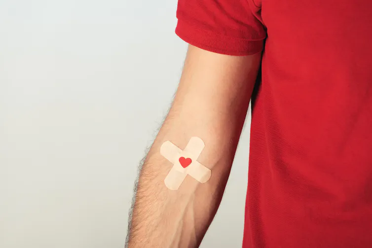 Person in red T-shirt wearing a criss-cross plaster and a red heart symbol over it on their arm