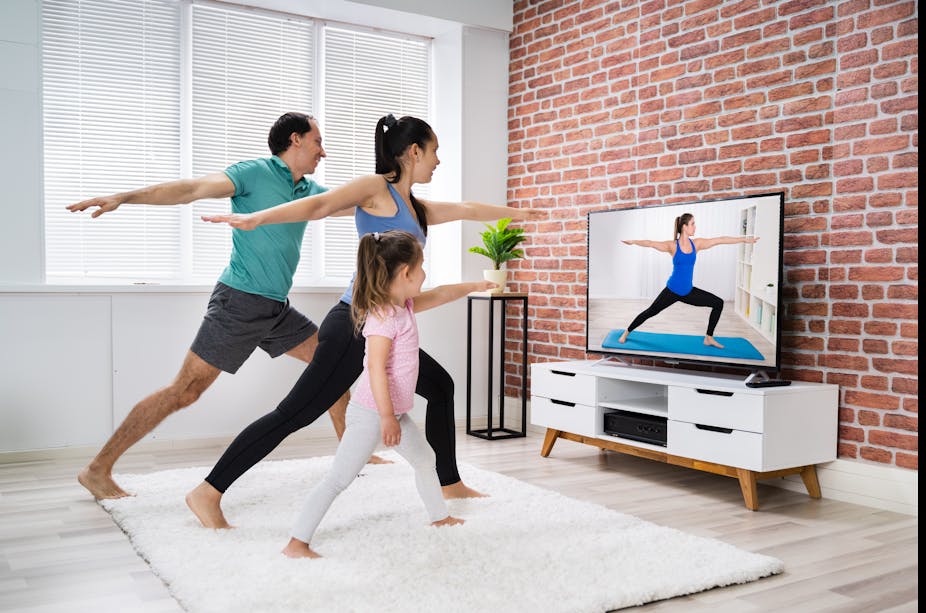 A father, mother, and young girl do yoga together in their home.