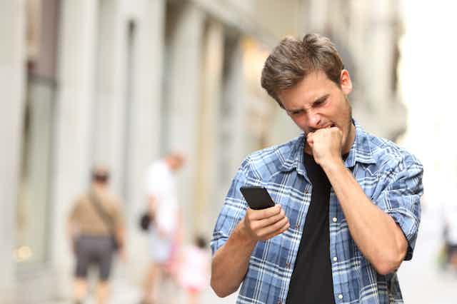 Un hombre se muerde el puño mientras mira furioso su teléfono móvil.