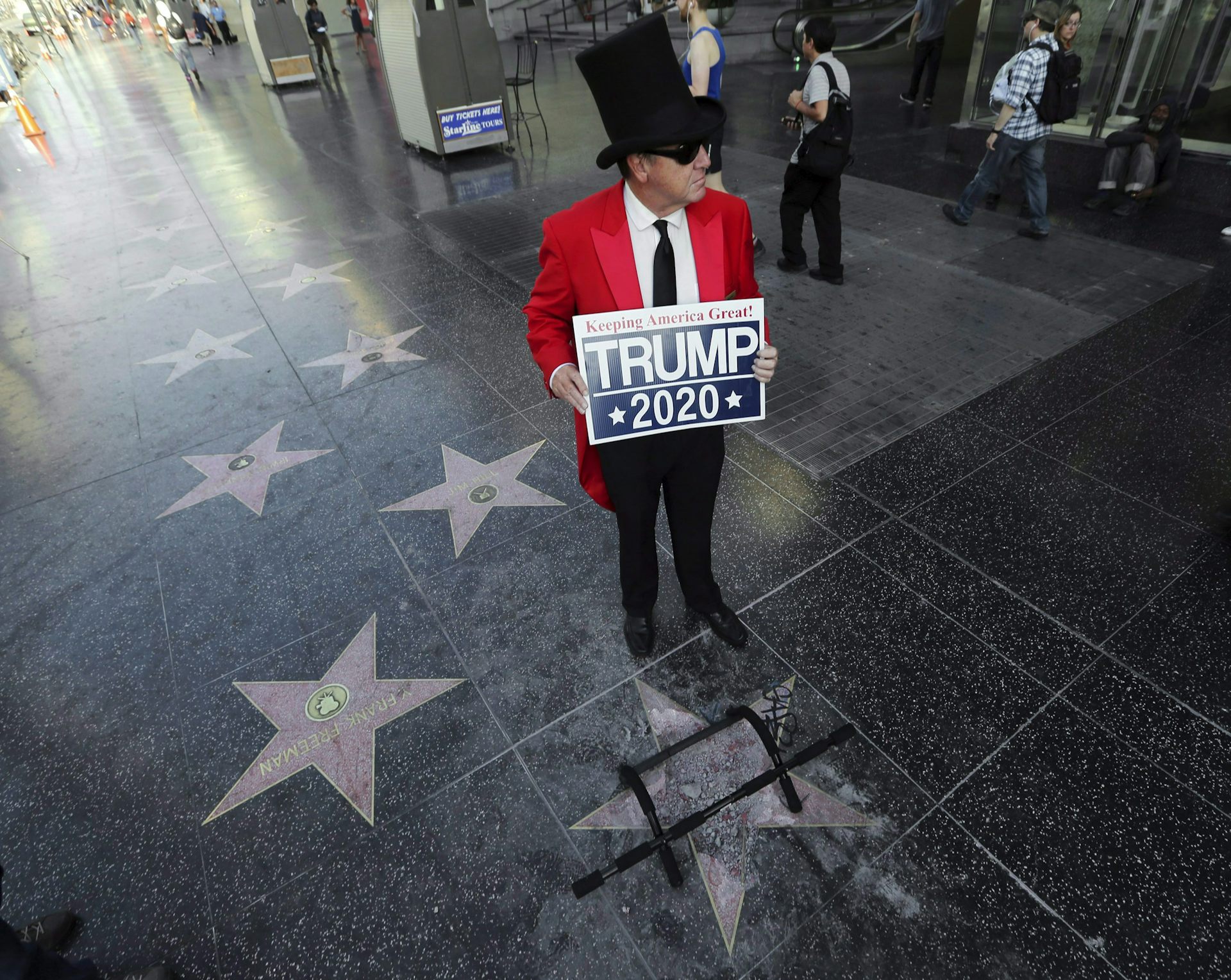 A Trump supporter carrying a Trump 2020 sign stands near the president's vandalized star on the Hollywood Walk of Fame.