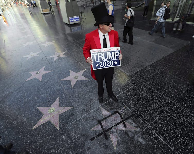 A Trump supporter carrying a Trump 2020 sign stands near the president's vandalized star on the Hollywood Walk of Fame.