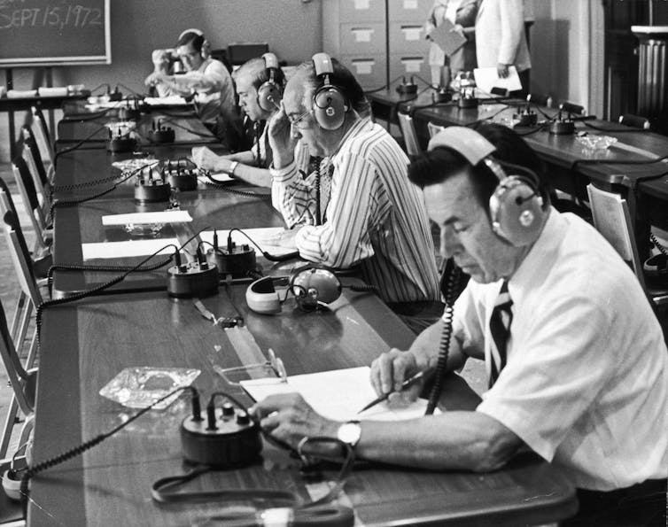 Legislators at a long table wearing headphones.