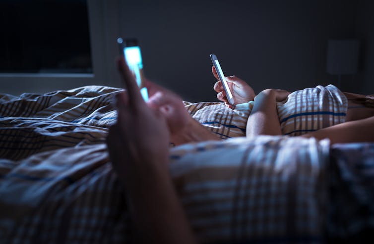 Couple in bed looking at smartphones.