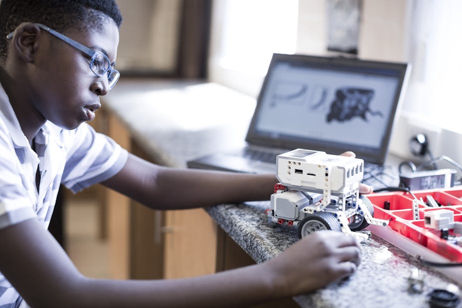 A boy wearing glasses builds a small robot.