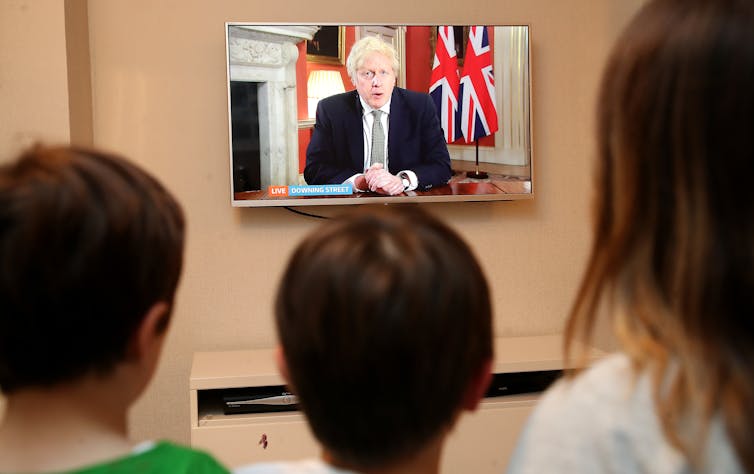 A family watches a TV screen as the prime minister announce lockdown measures.