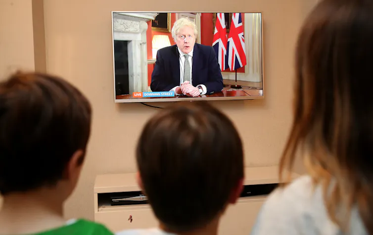 A family watches a TV screen as the prime minister announce lockdown measures.