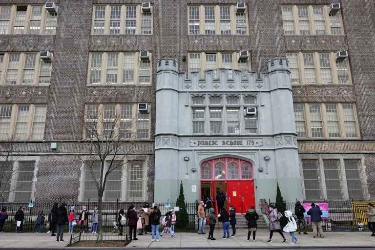 Adults and children stand outside a large brick building