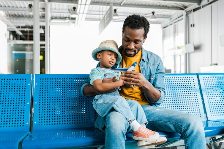 Father holds child with plane figurine on his lap at airport