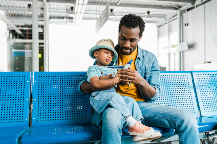 Father holds child with plane figurine on his lap at airport