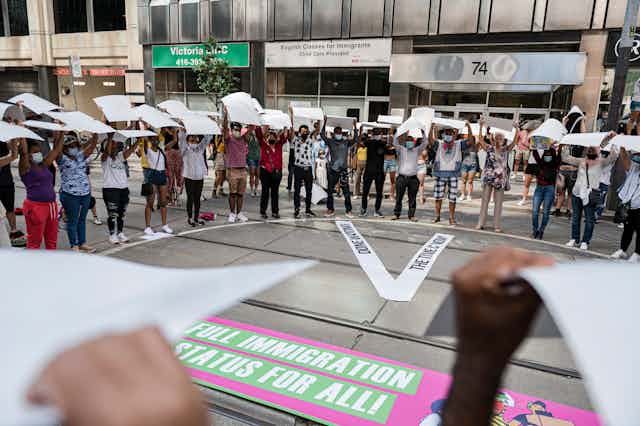 Protesters gather in a circle surrounding a banner that reads: full immigration status for all