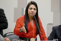 Woman in a red shirt speaking at a microphone