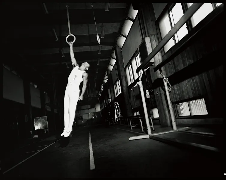 Yukio Mishima, vêtu de blanc, est suspendu, ensanglanté, à un anneau immobile.