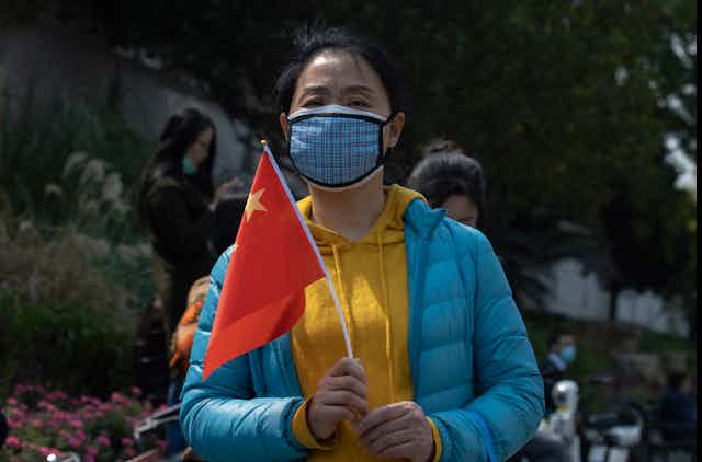 A woman outdoors wearing a mask holds a Chinese national flag