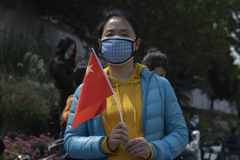 A woman outdoors wearing a mask holds a Chinese national flag