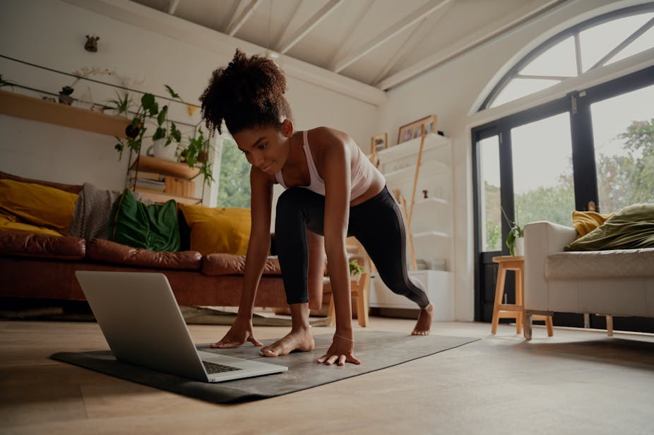 Young woman exercising at home with a video on her laptop.