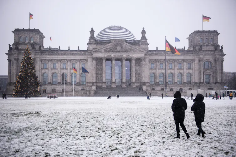 Two people walk past Berlin's Reichstag in the snow.