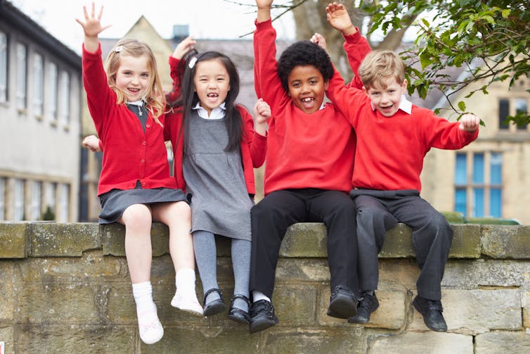 Schoolchildren sitting together on wall.