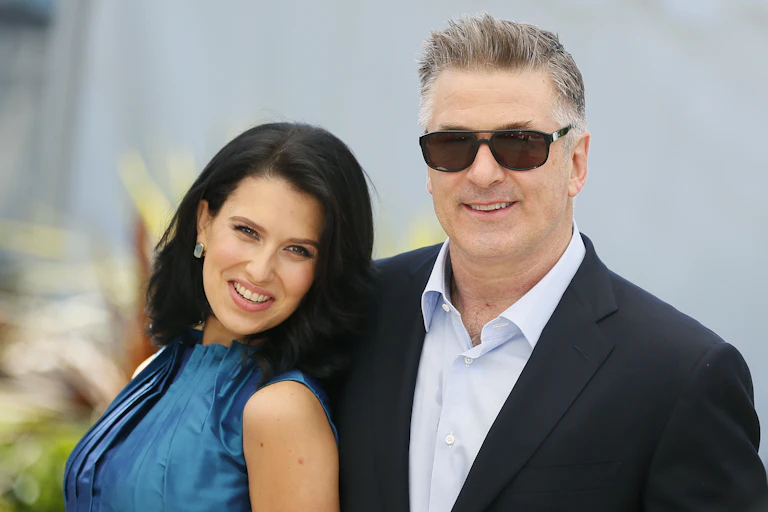 Woman with long dark hair in blue dress alongside man in lounge suit and open-necked shirt wearing sunglasses.