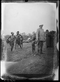 Officier colonial tenant la main d’un enfant dans un village africain, 1904-1914.