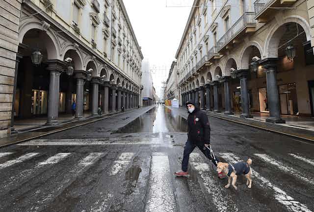 A man wearing a mask walks a dog throgh Turin.