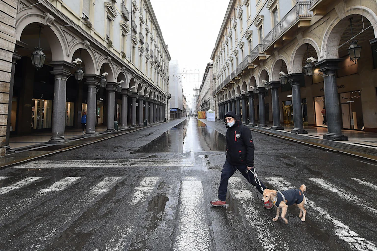 A man wearing a mask walks a dog throgh Turin.