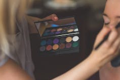 A makeup artist applies eye shadow to another woman.