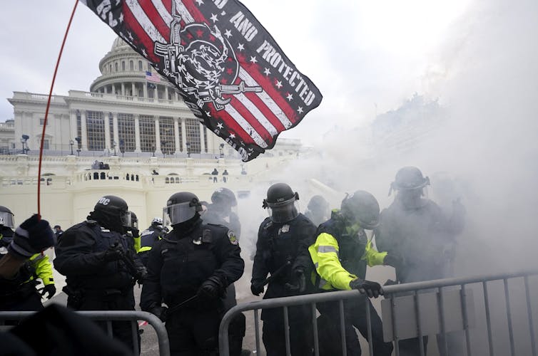 Police in riot gear are behind a metal barricade in front of the Capitol dome