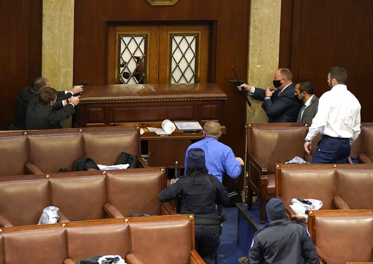 Capitol police officers point their guns at a vandalized door, barricaded to prevent entry.