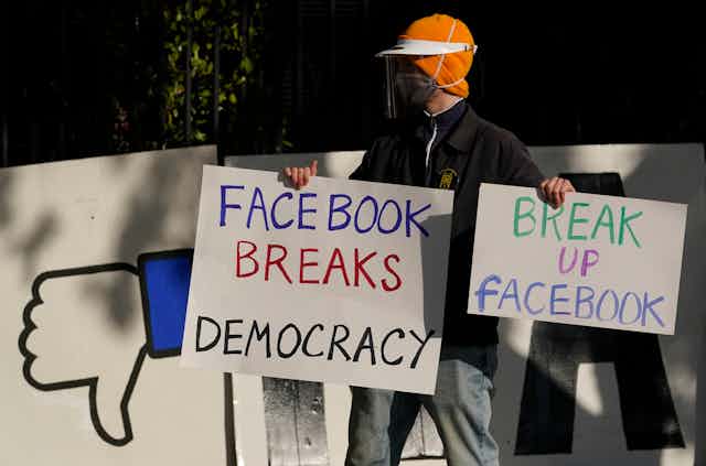 A man wearing a mask carries anti-Facebook signs calling for the tech giant to be broken up.