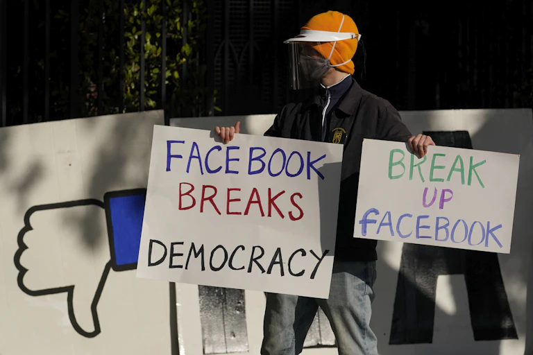 A man wearing a mask carries anti-Facebook signs calling for the tech giant to be broken up.