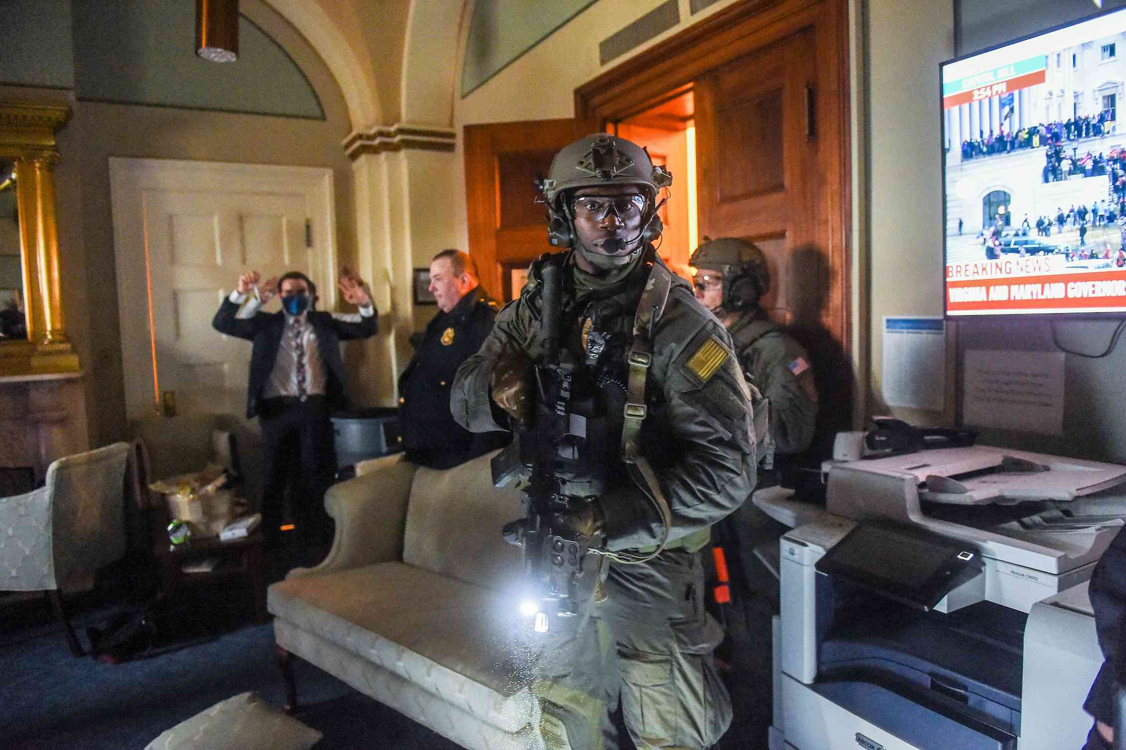 Un empleado del Congreso mantiene las manos arriba mientras un miembro de un equipo SWAT de la Policía del Capitolio despeja una habitación Los equipos SWAT tratan de liberar el edificio del Capitolio de manifestantes pro-Trump. Olivier Douliery/AFP via Getty Images