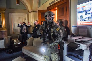 Un membro del Congresso tiene le mani alzate mentre la squadra SWAT della polizia di Capitol ripulisce un ufficio