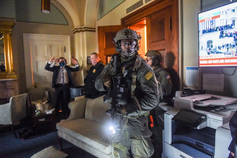 Un empleado del Congreso mantiene las manos arriba mientras un miembro de un equipo SWAT de la Policía del Capitolio despeja una habitación
