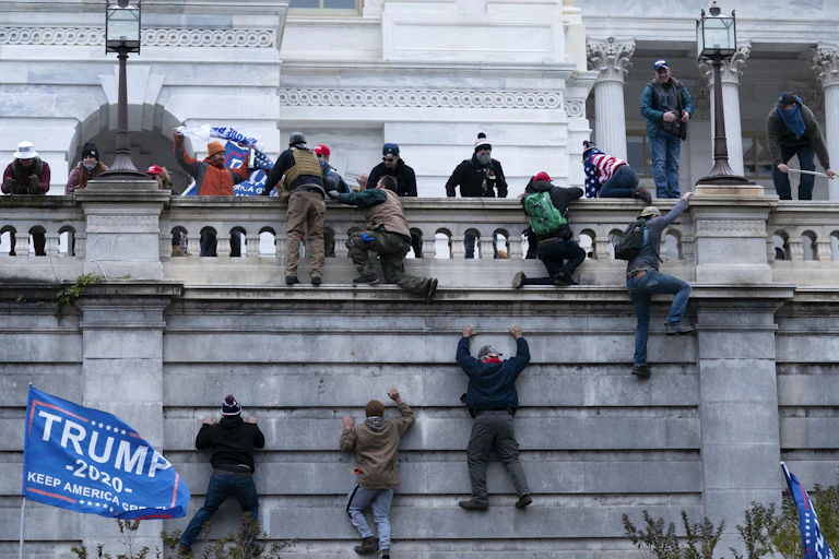 Protesters climbing a wall into Capitol building