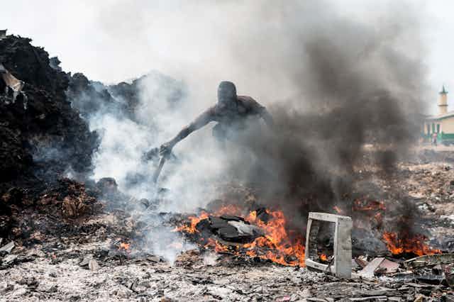 A man sorts burning electronic waste in a dumpsite.