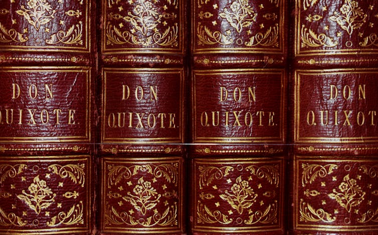 Red hard-bound editions of Miguel de Cervante’s Don Quixote books in a row on a shelf