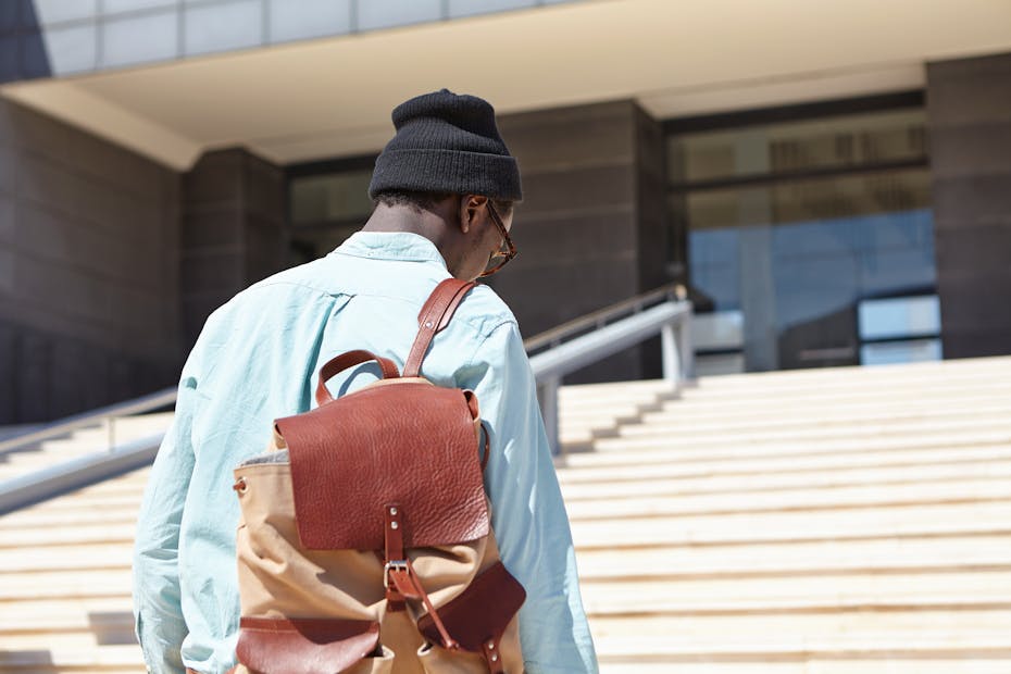 Young man with rucksack walking alone up steps to modern building