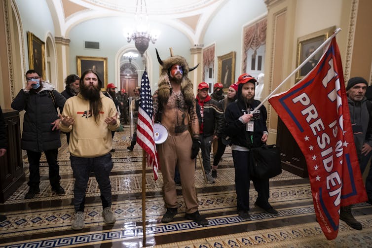 Group of men in various outfits, some carrying flags inside the Capitol in Washington DC, January 2021.