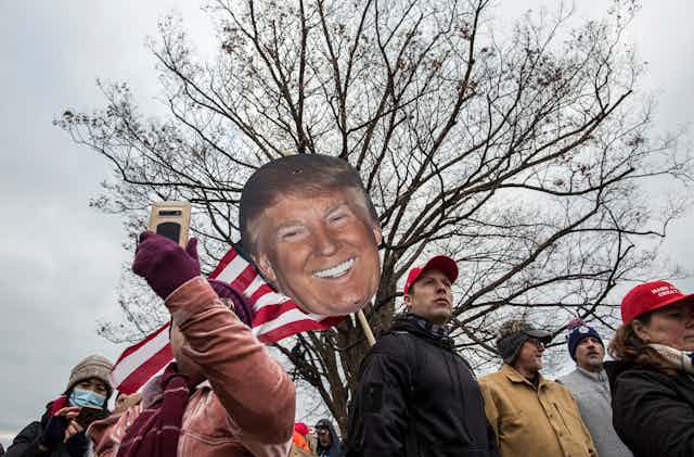 MAGA crowd marches with cardboard cutout of Trump's face