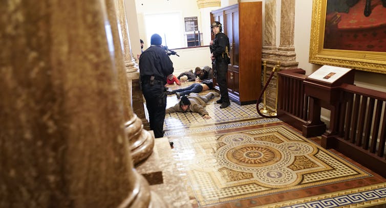 Police hold protesters at gunpoint as they lie on a marble floor.