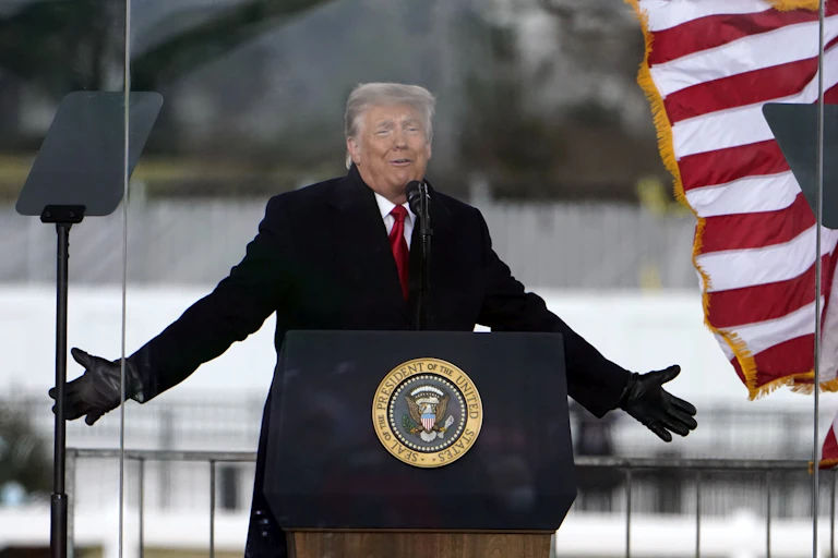 President Trump extends his arms as he speaks at a podium with the presidential seal.