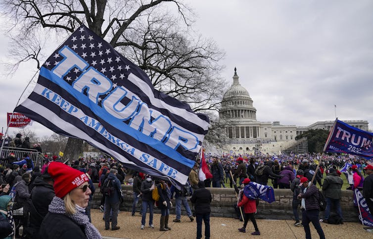 The U.S. Capitol dome is in the background as a large Trump flags flaps in the foreground near protesters.